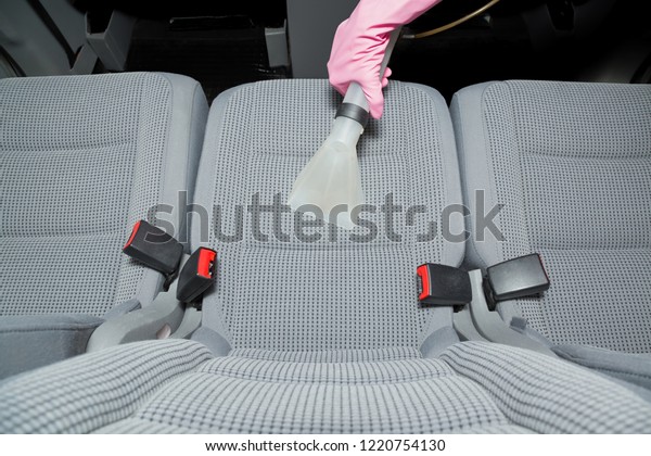 Cleaner hand in protective glove cleaning gray\
textile back passenger seat with professionally extraction method.\
Regular cleanup. Care about auto interior. Commercial cleaning\
company. Top view.