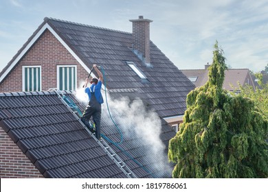 Cleaner with pressure washer at roof of house cleaning the roof tiles, removing moss and weed