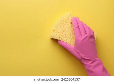 Cleaner in rubber glove holding new sponge on yellow background, top view. Space for text - Powered by Shutterstock