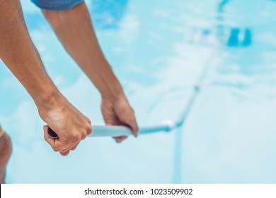 Cleaner of the swimming pool . Man in a blue shirt with cleaning equipment for swimming pools, sunny.