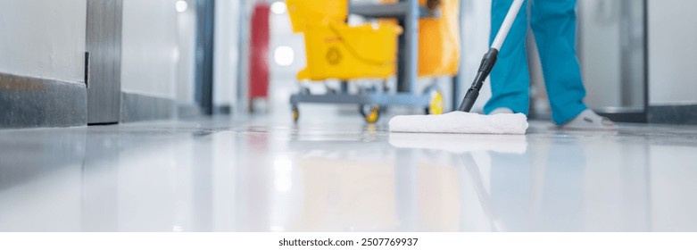 A cleaner in uniform efficiently mops the epoxy floor in the patient room, ensuring the hall floor is free from any dirt or germs.