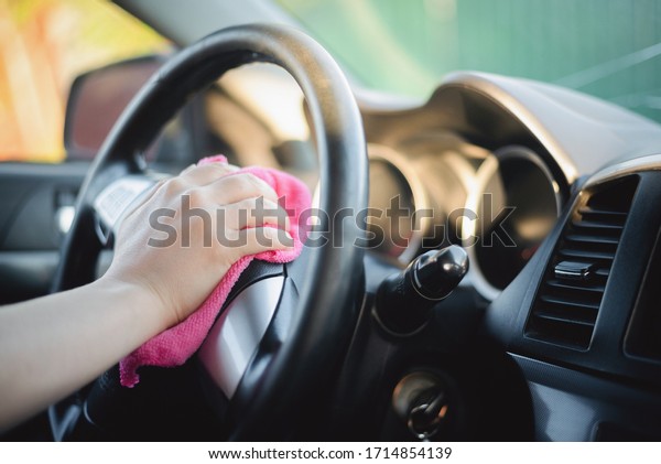 The cleaner wipes and polishes the car steering wheel\
with a rag close up.