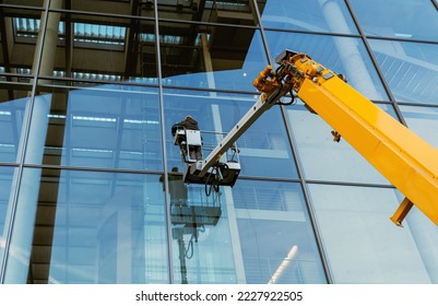 Cleaner worker using a cherry picker to clean a glas facade of a contemporary office building.