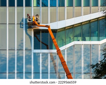 Cleaner worker using a cherry picker to clean a glas facade of a contemporary office building.