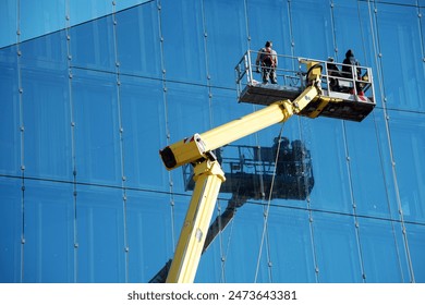 Cleaner worker using a cherry picker to clean a glas facade of a contemporary office building.