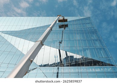 Cleaner worker using a cherry picker to clean a glas facade of a contemporary office building.
