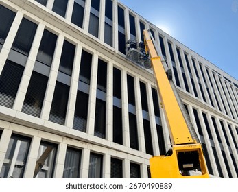 Cleaner worker using a cherry picker to clean a glas facade of a contemporary office building.