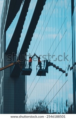 Cleaner worker using a cherry picker to clean a glass facade of a contemporary office building. A worker washes the windows of a house from a platform on a crane.