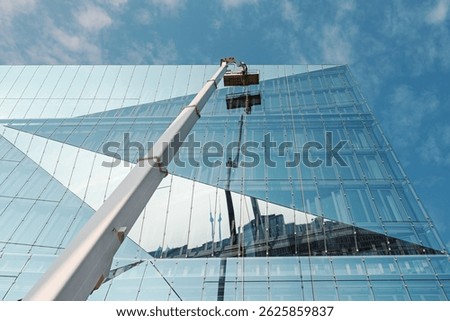 Cleaner worker using a cherry picker to clean a glas facade of a contemporary office building.