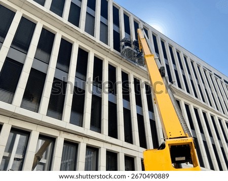 Cleaner worker using a cherry picker to clean a glas facade of a contemporary office building.