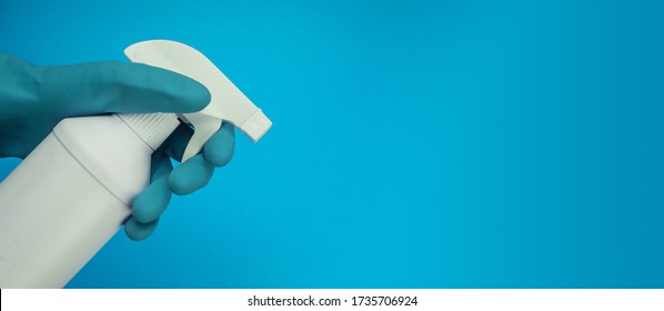 Cleaner's Hand In Blue Rubber Protective Glove Holding Achemical Spray Bottle. Empty Place For Text Or Logo On Gray Background. Early Spring Or Regular Cleanup. Commercial Cleaning Company 