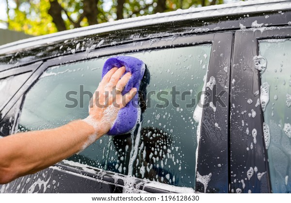 Cleaning automobile Using High Pressure\
Water. Man washing his car under high pressure water in\
service.worker washing car.Protection of car concept.male hand with\
purpl sponge washing\
auto.Selective