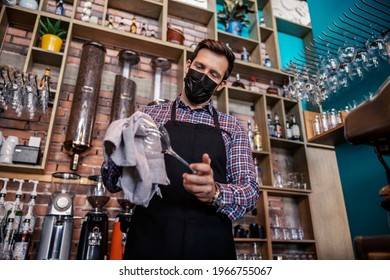 Cleaning The Bar In The Restaurant. An Adult Handsome Man In A Waiter's Uniform Stands Behind The Bar And Wipes Freshly Washed Wine Glasses With A Cloth. Restaurant Work And Corona Virus