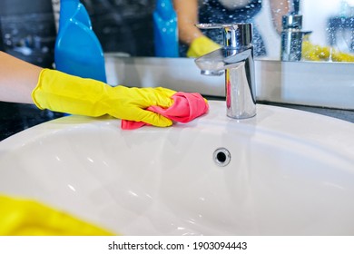 Cleaning the bathroom. Close up of hands in gloves with detergent and microfiber cloth washing polishing washbasin