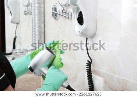Cleaning the bathroom. The maid wipes the hair dryer. The concept of cleaning in a house or hotel. Hands in protective gloves.