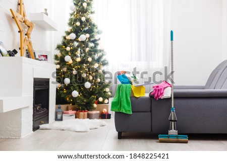 Cleaning before Christmas. Multicolored cleaning supplies. Sponges, rags and spray with festive decorations against modern home background