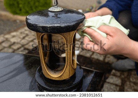 Cleaning a black tombstone with a cloth and water, female hands visible.