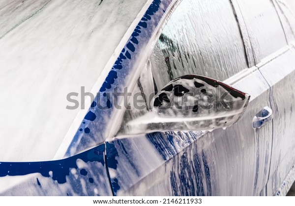 Cleaning of blue automobile with soap and\
pressurized water jet at car wash service. Electric vehicle washed\
in garage close view