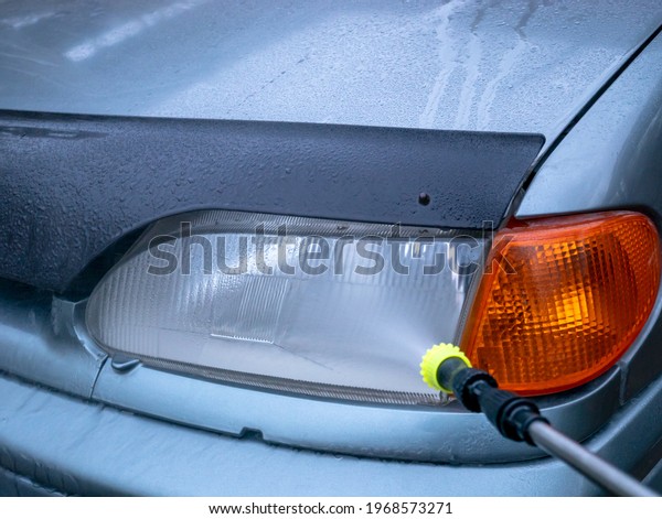 Cleaning car headlights with a high pressure\
washer close-up. Car wash with\
water.