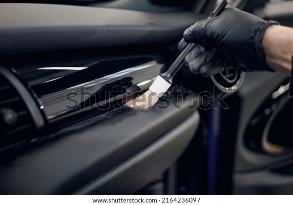 Cleaning the car\
interior with a brush. Auto detailing worker cleaning car interior,\
car detailing concept. Selective focus. Dust removal from the\
dashboard of the car with a\
brush
