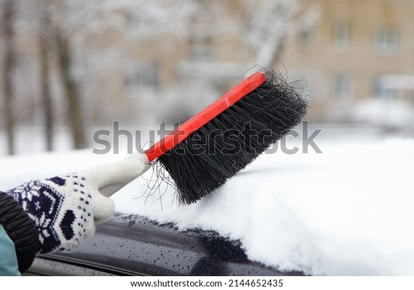 Cleaning the car roof from snow with a brush in\
winter after snowfall in\
Europe