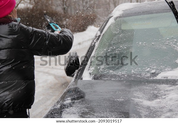 Cleaning the car from snow with a brush\
close-up. Snowfall