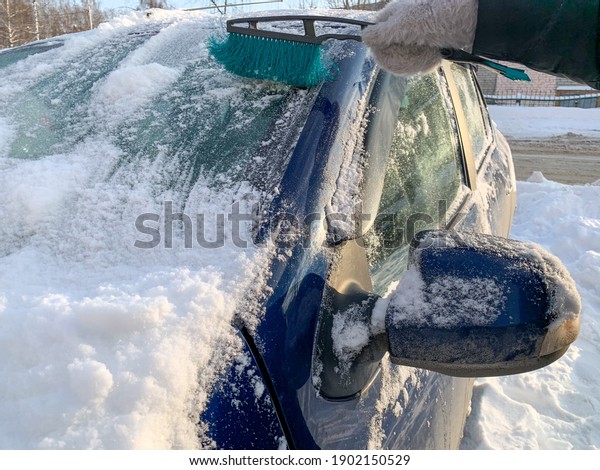 Cleaning the car from snow with a\
brush. In the photo, the girl cleans the car from the snow. Snow\
removal, keeping the car clean. Winter weather,\
snowfall