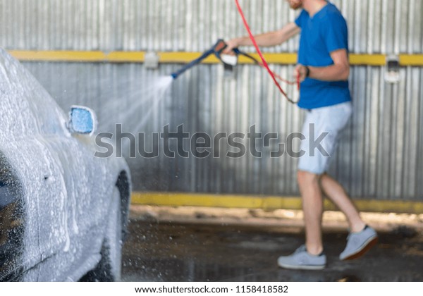 Cleaning Car Using High Pressure Water. Man washing\
his car under high pressure water in service.  Washing car with\
soap