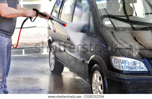 Cleaning Car Using High\
Pressure Water. Man washing his car under high pressure water in\
service