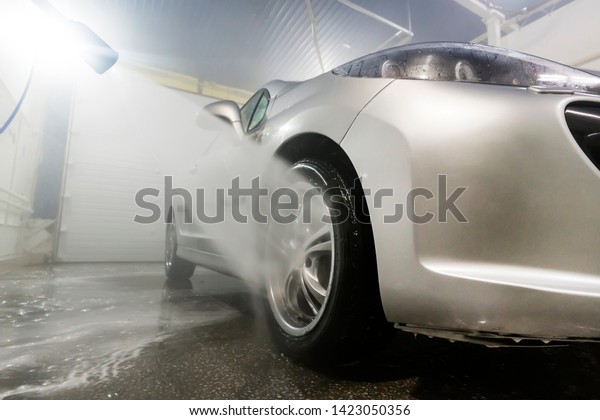 Cleaning Car Using High Pressure Water. Man\
washing his car under high pressure water in service. man worker\
washes the car.\
self-service