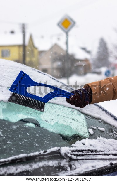 Cleaning car\
windshield from snow by ice scraper with brush at winter. Remove\
snow from car on the\
street.