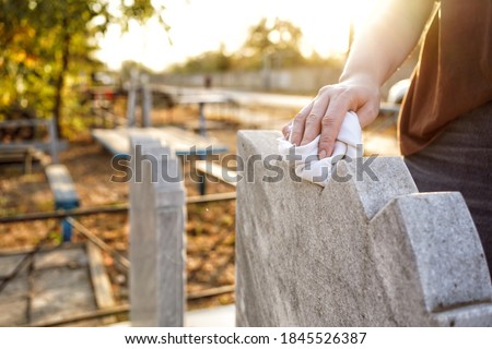 Cleaning the cemetery. A woman's hand washes the grey monument at the grave with a rag. Parents Saturday in Russia. business beautification of the graves.