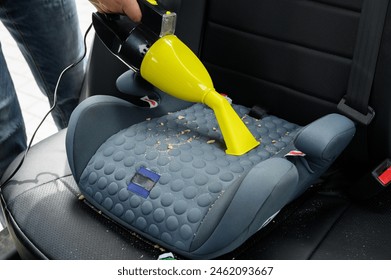 Cleaning child booster seat with vacuum cleaner. Car wash worker cleans seat from crumbs ,debris left after child ride in car. Concept of maintaining cleanliness in car interior, cleaning company.  - Powered by Shutterstock