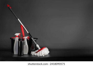 Cleaning concept mop and bucket. Cleaning products and spin mop with red details on the floor in the grey-black background. Empty blank copy space - Powered by Shutterstock