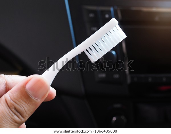 Cleaning the control panel inside the car with\
a white toothbrush