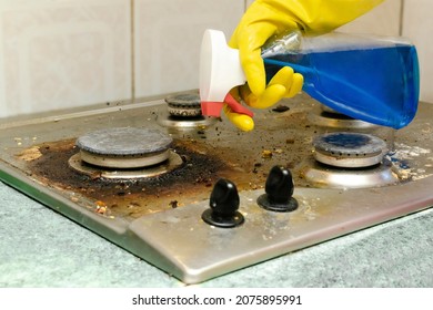 Cleaning Dirty Gas Stove From Grease, Food Leftovers Deposits. Woman's Hand In Protective Glove With Sponge Rag And Detergent In Bottle Washing Kitchen Stove. Home Cleaning Service Concept.