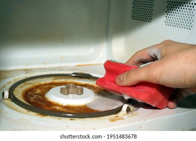 Cleaning A Dirty Microwave Oven. A Hand With A Sponge And Washing Foam Cleans The Microwave From Grease And Dirt