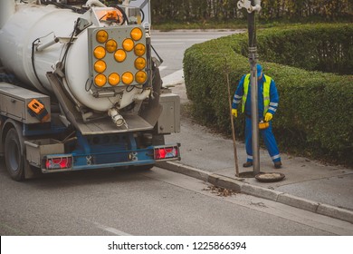 Cleaning drainage pipes of leaves and debris with a big vacuum tank truck. Unrecognisable worker cleaning water drains on the street.