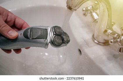 Cleaning the electric shaver mesh under running water in the faucet. Clean the beard shaving machine under water. - Powered by Shutterstock