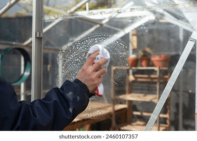 Cleaning the empty greenhouse with an antibacterial cleaner liquid, gardener spray it on the greenhouse wall for disinfection. Spring gardening work concept - Powered by Shutterstock