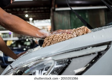 Cleaning the front hood of a white car with a microfiber wash mitt soaked in shampoo to lift grime and dirt. At a carwash or auto detailing shop. - Shutterstock ID 2055351086