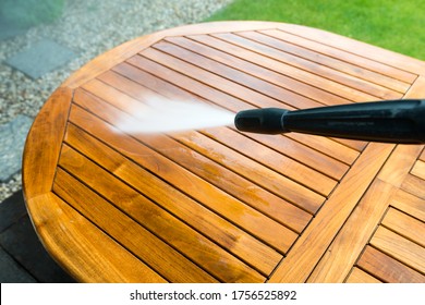 cleaning garden table with a power washer - high water pressure cleaner on wooden exotic table surface  - focus on the tip of the spray nozzle