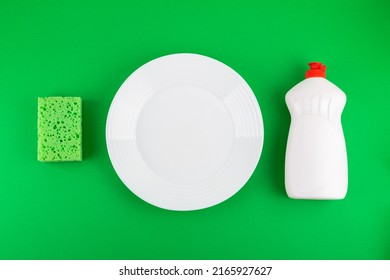 Cleaning green sponge, white plate and detergent for dishes on a green background. Top view, flatlay, close up. Concept cleaning company, purity, cleaning, kitchen