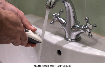 Cleaning the hair clipper under a stream of water in the faucet. Shaving hair at home. Rinse the blades under the tap - Powered by Shutterstock