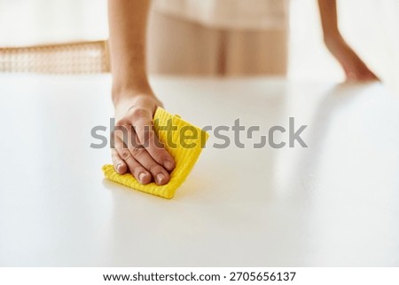Cleaning hands wipe white table with yellow cloth, household surface cleaning and tidy home. Closeup of person wiping kitchen or dining table for hygiene and neatness.