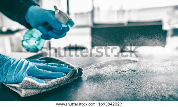 Cleaning home table sanitizing kitchen\
table surface with disinfectant spray bottle washing surfaces with\
towel and gloves. COVID-19 prevention sanitizing\
inside.
