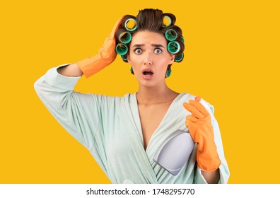 Cleaning House. Confused Housewife Holding Detergent Bottle Touching Head Looking At Camera In Shock Posing Over Yellow Background. Studio Shot