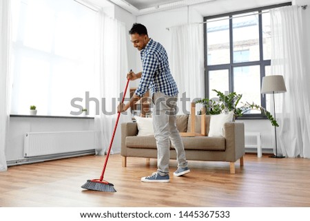 cleaning, housework and housekeeping concept - indian man with broom sweeping floor at home