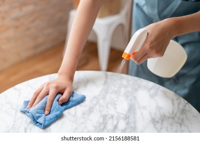 Cleaning hygiene, asian young maid woman, girl hand in using a water sprayer bottle to wipe clean, use blue rag wiping to dust on white marble table in restaurant. Housekeeping cleanup, cleaner.