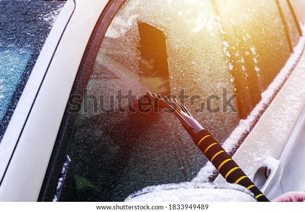 Cleaning an icy\
window on a car with ice scraper. Snow scraper. Cold snowy and\
frosty morning. Frozen car\
window.
